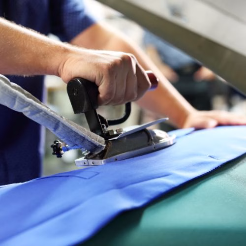 Worker ironing a blue garment in a professional clothing factory for quality finishing.