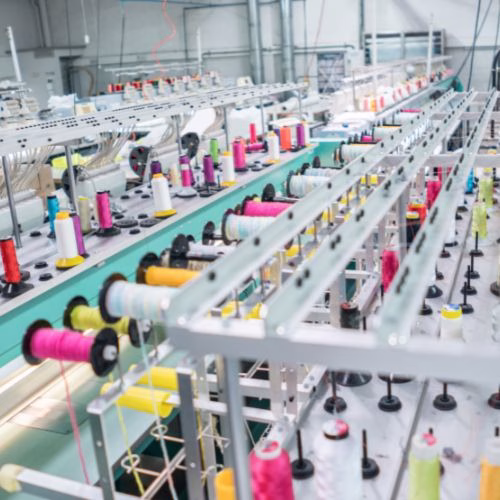 Rows of colorful thread spools on industrial machines in a clothing manufacturing factory.